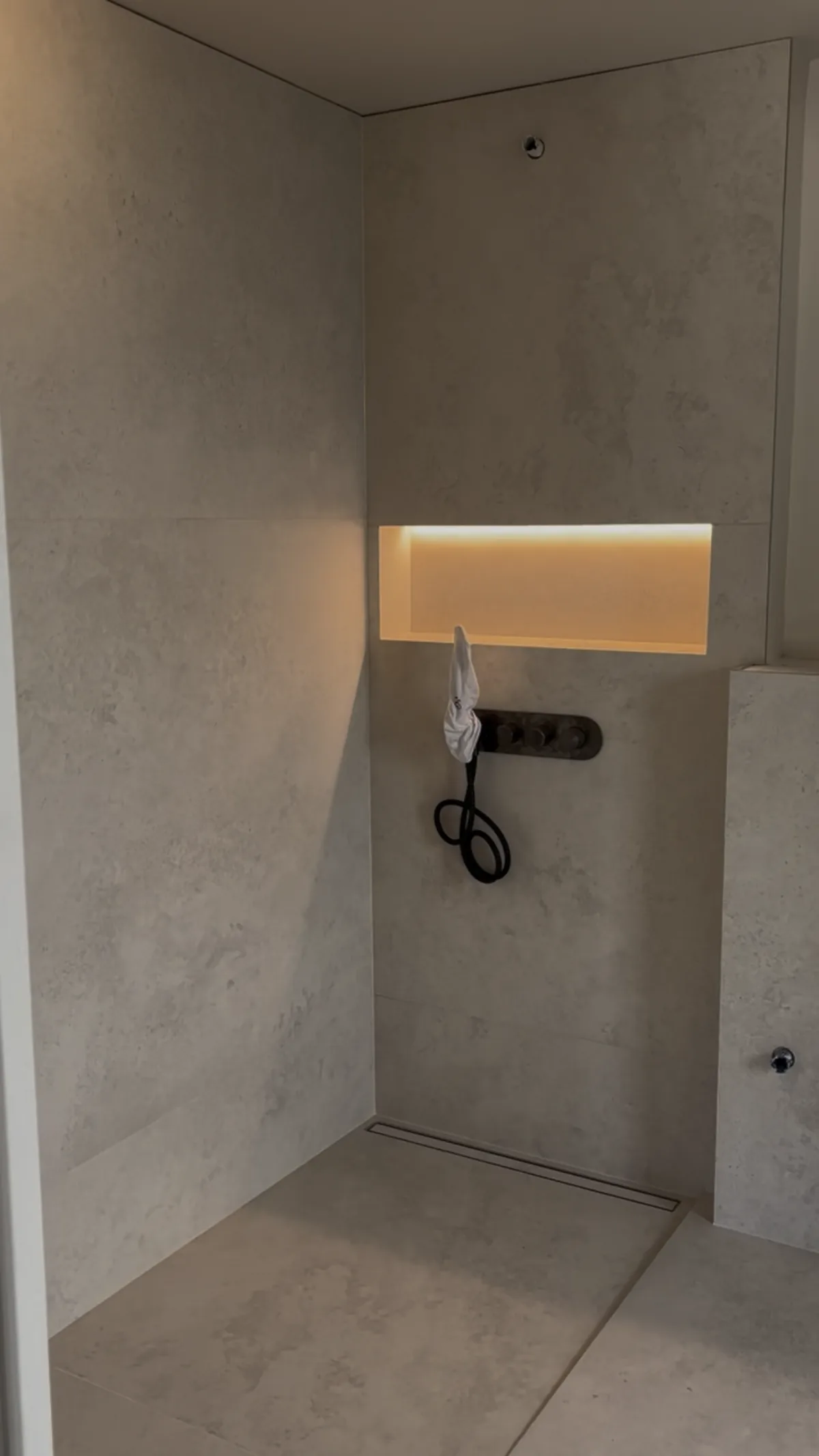 Douche à l'italienne en carrelage grand format effet béton, niche murale rétroéclairée.