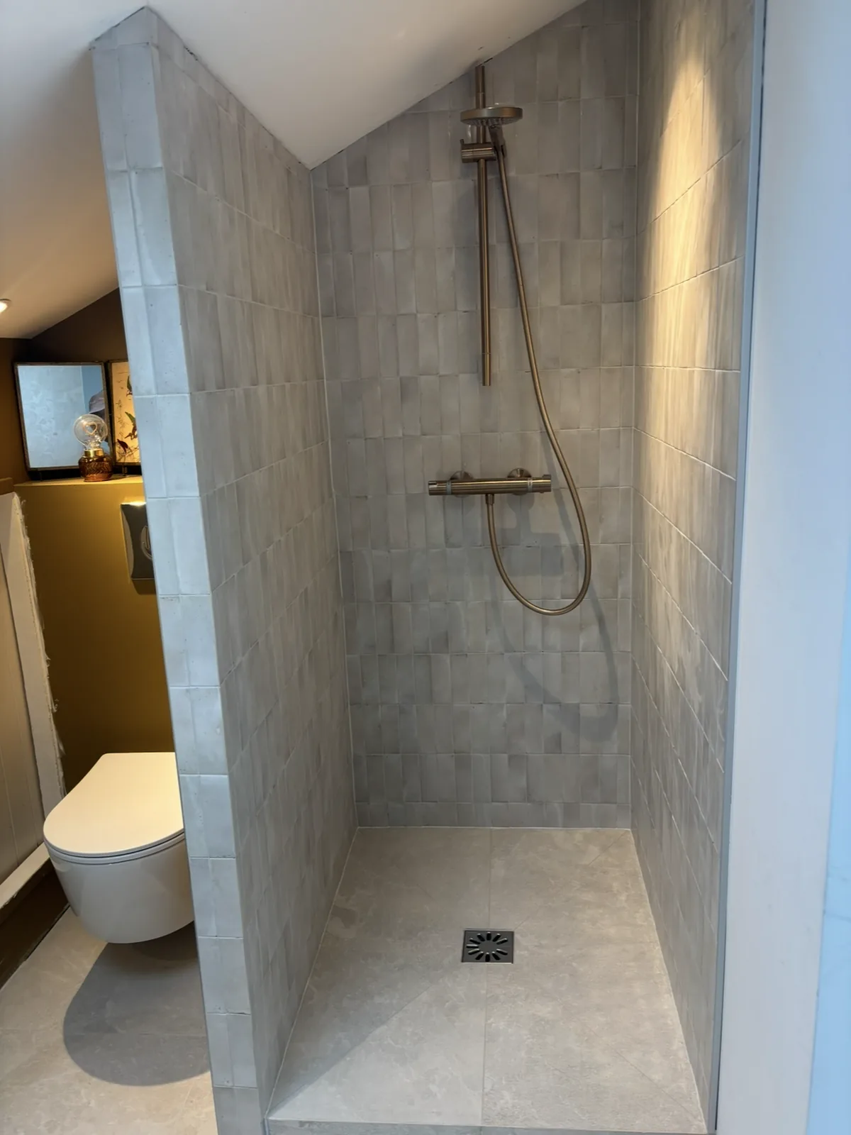 Douche à l'italienne avec faïence murale verticale effet zellige gris, receveur en carrelage grand format et évacuation encastrée.
