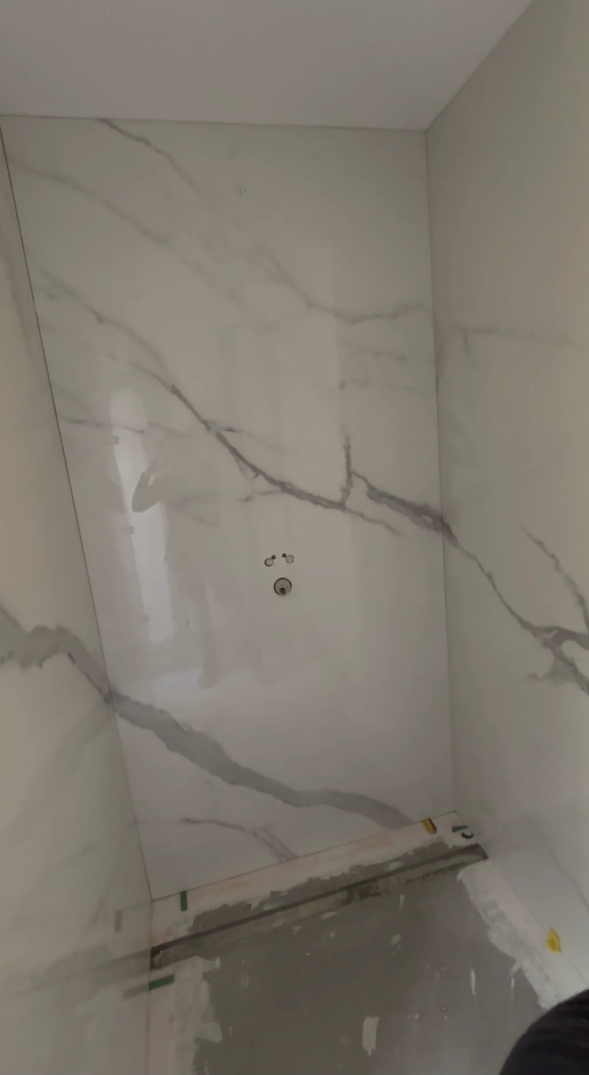 Angle de douche en carrelage grand format effet marbre blanc veiné, pose ajustée au millimètre entre les deux pans.